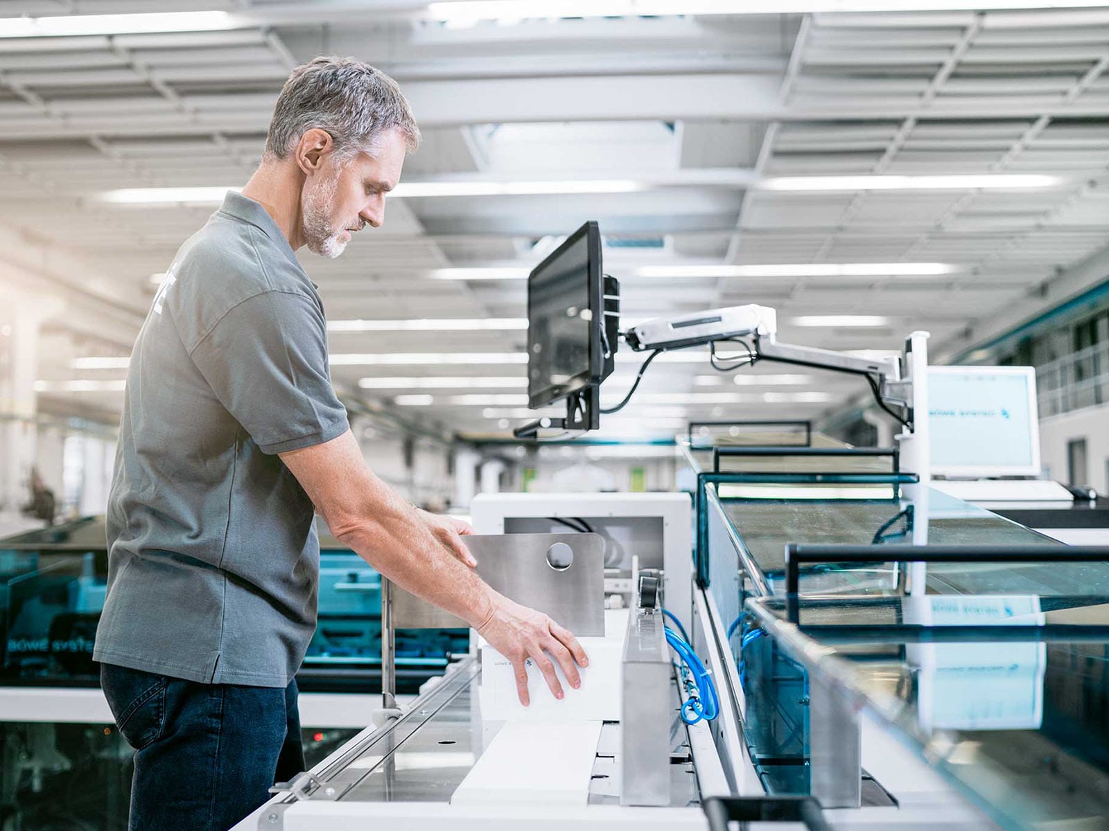 Industrial Worker Operating Machinery in a Modern Facility A male industrial worker using machinery in a large, well-lit factory setting, focusing on a piece of equipment with a monitor.